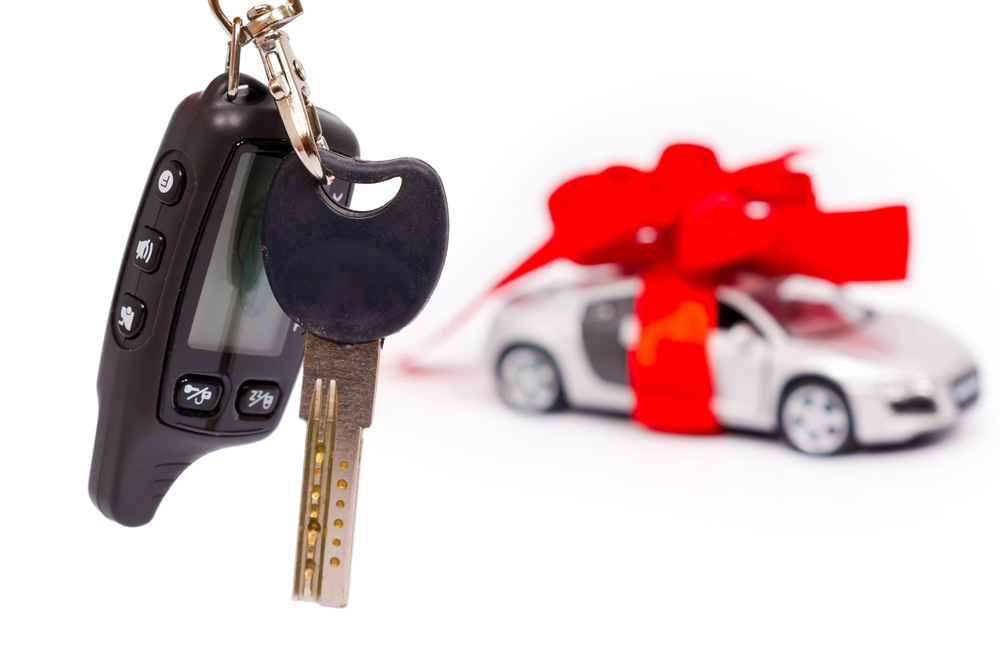 Car keys on the background of the machine with a red bow isolated on white background. Gift